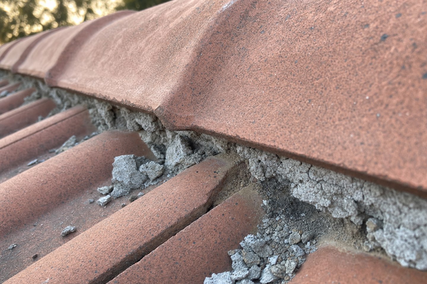 Macro photo of crumbling, powdery mortar bedding under a concrete ridge capping tile