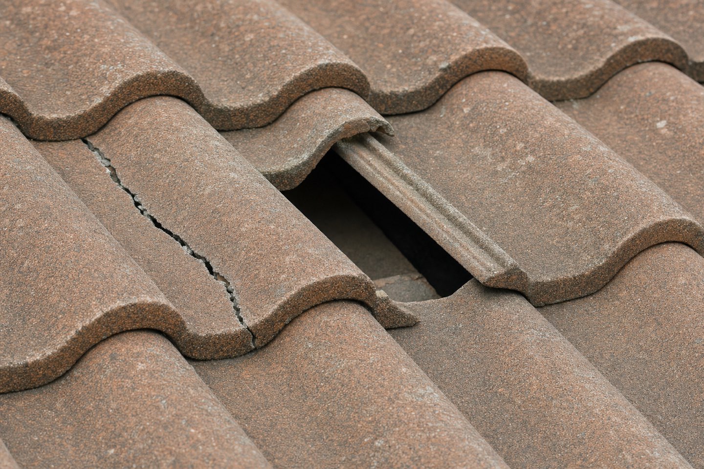 Macro photo of one cracked concrete roof tile and one slipped tile with a dark gap beneath