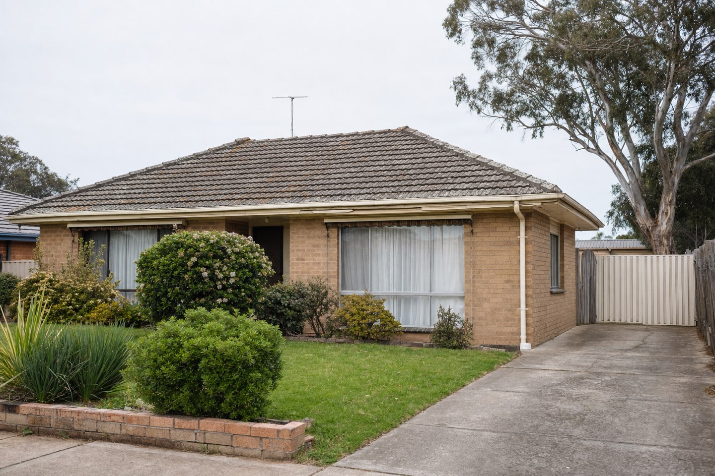 A 1990s brick home with a faded, moss-blotched tile roof before restoration